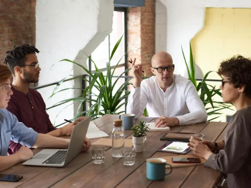 A diverse group of professionals of various ages sitting around a table in an office, engaged in a discussion about a project.
